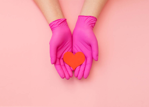 Close-up of hands in pink protective hold red heart. Cardiology concept. - 写真・画像