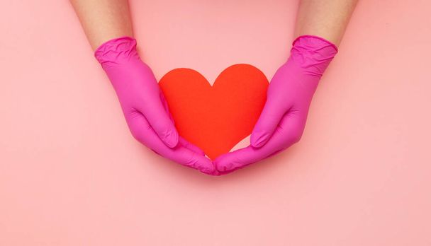 Close-up of hands in pink protective hold red heart. Cardiology concept. - Zdjęcie, obraz
