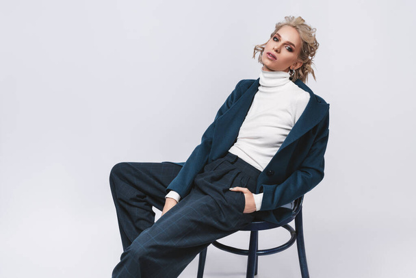 Fashion photo of a beautiful woman with blond nice hairstyle wearing  blue suit.Female beauty concept.Portrait of fashionable young girl dressed just in classic jacket posing over gray background - Photo, Image
