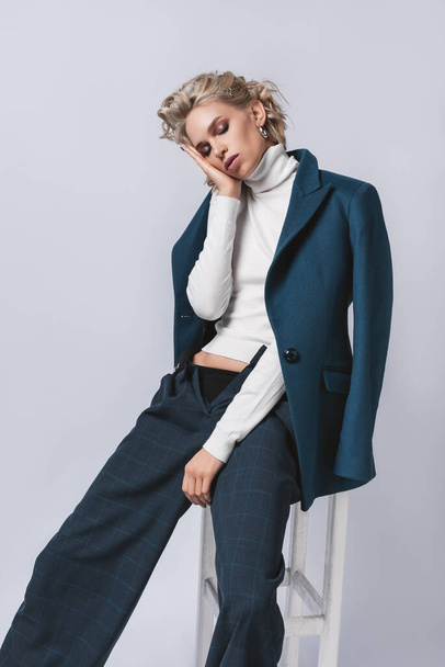 Fashion photo of a beautiful woman with blond nice hairstyle wearing  blue suit.Female beauty concept.Portrait of fashionable young girl dressed just in classic jacket posing over gray background - Zdjęcie, obraz
