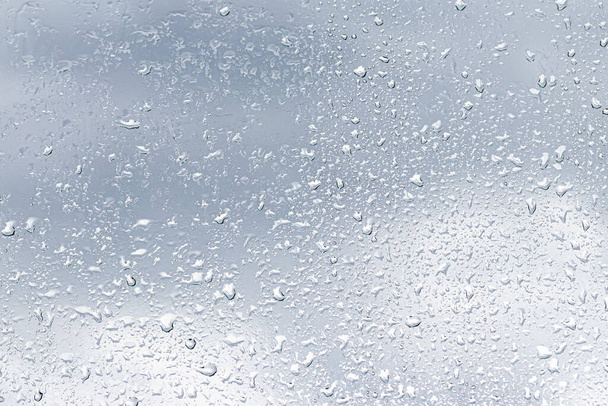 Gotas de lluvia en la superficie de los cristales de la ventana con fondo nublado. Fondo natural de gotas de lluvia. Superposición abstracta para el diseño. El concepto de mal tiempo lluvioso
. - Foto, imagen