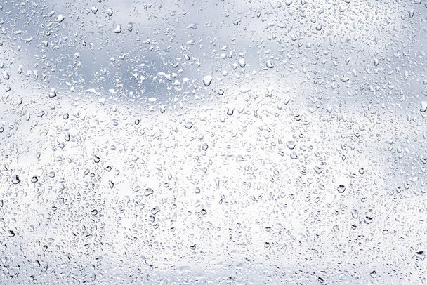 Rain drops on window glasses surface with cloudy sky background . Natural backdrop of raindrops. Abstract overlay for design. The concept of bad rainy weather. - Photo, Image