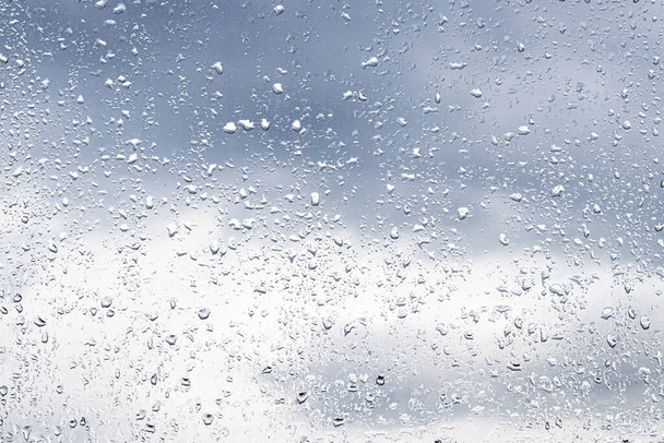 gouttes de pluie sur la surface des lunettes de fenêtre avec un fond nuageux. Fond naturel de gouttes de pluie. Superposition abstraite pour le design. Le concept de mauvais temps pluvieux. - Photo, image
