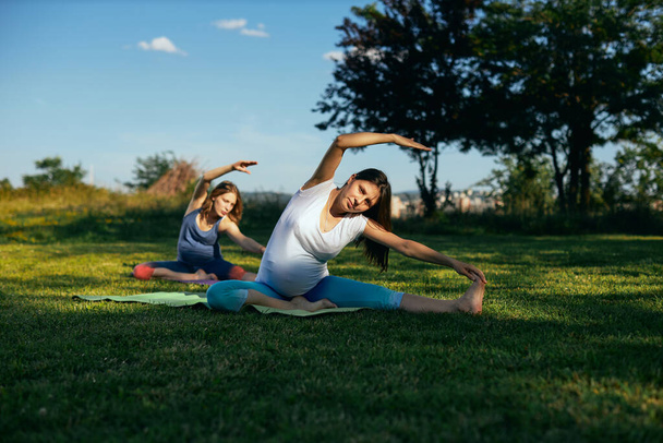 Zwei schwangere junge Frauen praktizieren Yoga im Freien. - Foto, Bild