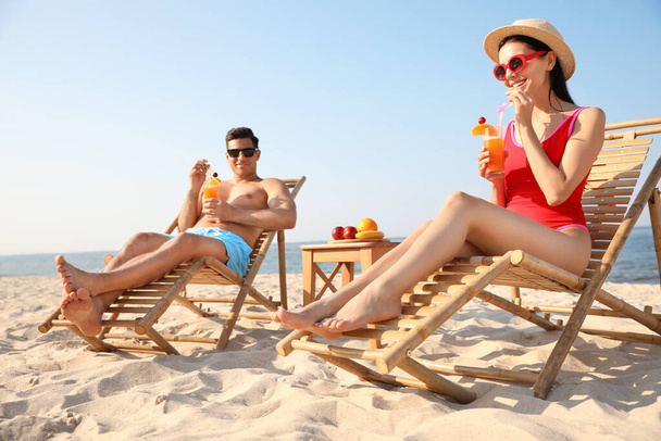Couple with drinks resting on sunny beach at resort - Photo, Image