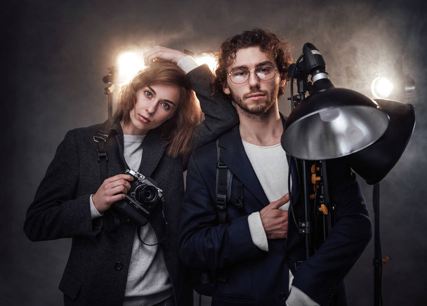 Команда двох фотографів тримає цифрову камеру та освітлювальне обладнання, позуючи в студії
 - Фото, зображення