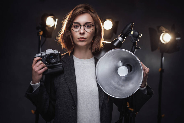 Hermosa pelirroja fotógrafa mujer sostiene una cámara digital y mirando a la cámara
 - Foto, Imagen