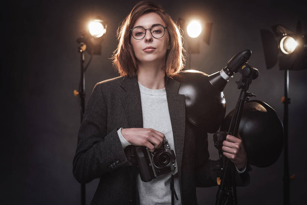 Όμορφη κοκκινομάλλα φωτογράφος κρατά μια ψηφιακή φωτογραφική μηχανή και κοιτάζοντας την κάμερα - Φωτογραφία, εικόνα