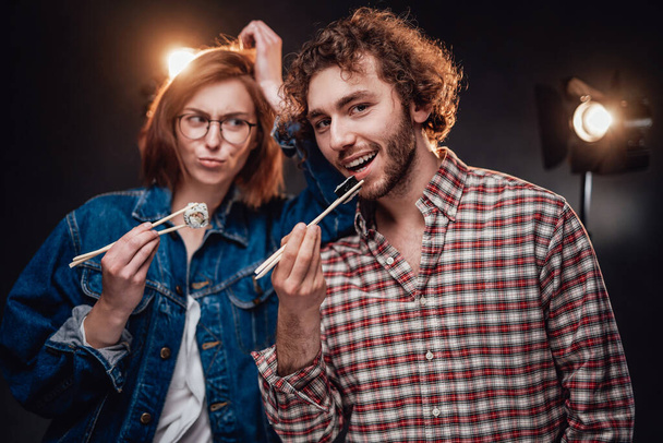 Bella giovane coppia alla moda gode di deliziosi rotoli di sushi in studio scuro - Foto, immagini