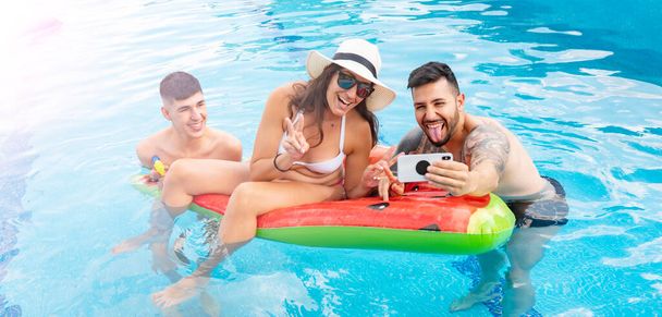 группа молодых людей, играющих в бассейне, концепция летних каникул, делающих селфи
 - Фото, изображение
