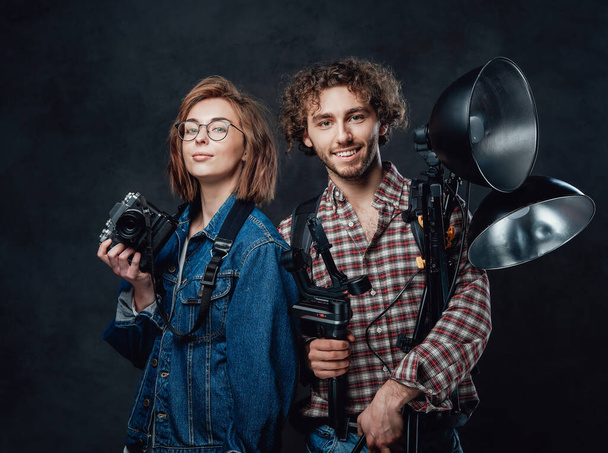 Das Team aus zwei jungen Fotografen hält eine Digitalkamera und Beleuchtungsgeräte im Studio - Foto, Bild