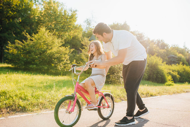 Young father teaching his daughter to ride bicycle - Fotoğraf, Görsel