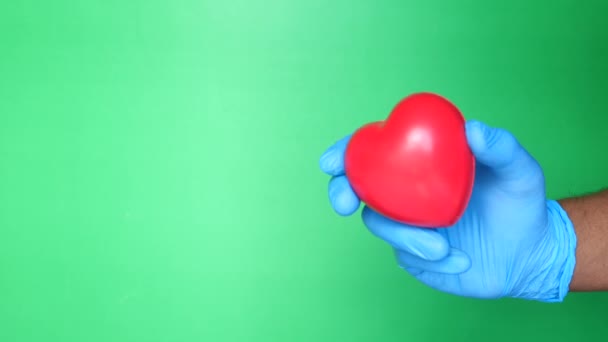 Médico mano en guantes médicos sosteniendo el corazón rojo sobre fondo verde
  - Metraje, vídeo
