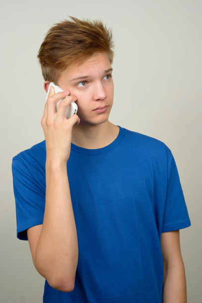 Studio shot of young handsome teenage boy against white background - Foto, afbeelding