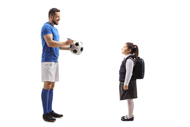 Full length profile shot of a footballer giving an autograph on a soccer ball to a schoolgirl isolated on white background - Zdjęcie, obraz