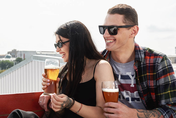 Happy smiling couple toasting and drinking beer at outdoor pub or bar on rooftop at summer, copy space - Photo, Image