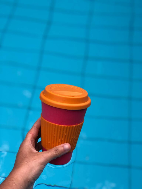 Γυναίκα απολαμβάνει τον καφέ σε μια επαναχρησιμοποιήσιμη κούπα μπαμπού στην πισίνα - Φωτογραφία, εικόνα