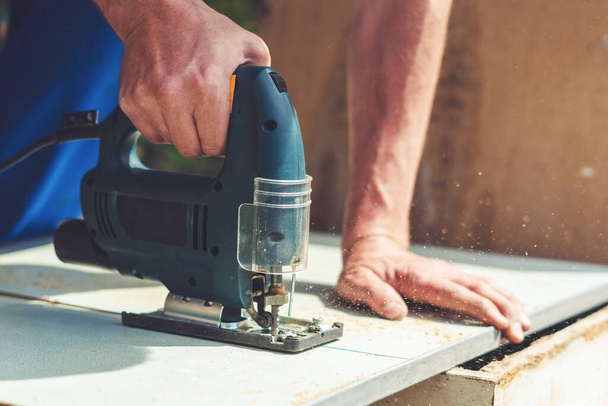 A carpenter saws a wooden cloth with an electric jig saw. - Фото, зображення