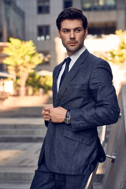 Young and successful. Handsome young man in full suit adjusting his jacket while standing outdoors - Foto, imagen