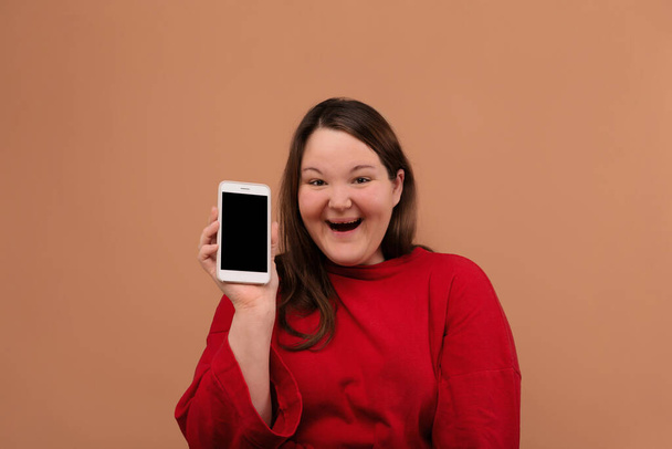 A beautiful overweight girl shows her mobile phone. With an empty screen. - Foto, afbeelding