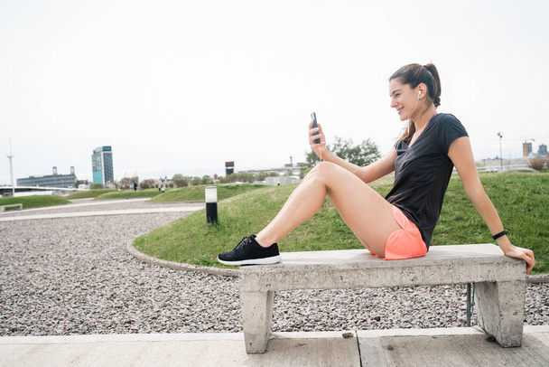 Retrato de uma mulher atlética usando seu telefone celular em uma pausa do treinamento. Desporto e estilo de vida. - Foto, Imagem