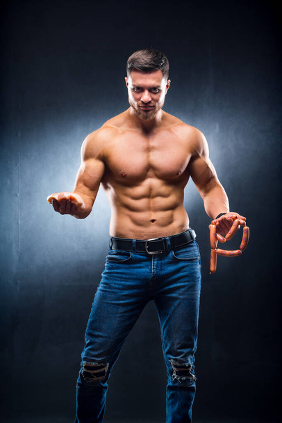 Athletic young sportsman holding chicken breasts and sausage. Dieting and sport nutrition, naked torso, muscular man. Cropped photo - Fotó, kép