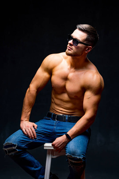 Athletic body. Half turned model guy is posing to the camera in the dark grey background. Full size photo. Strong muscular man. Closeup. - Foto, Imagem