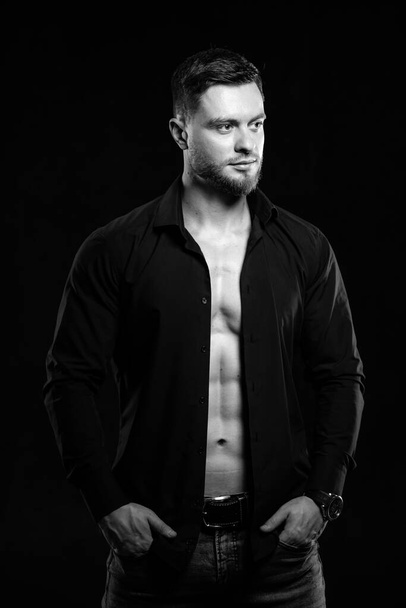 Muscular young man on dark background in fark unbuttoned shirt. Closeup. Black and white. - Foto, afbeelding