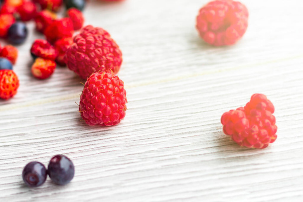 Wood background. Freshly picked blueberries, raspberries and wild strawberries - Фото, изображение
