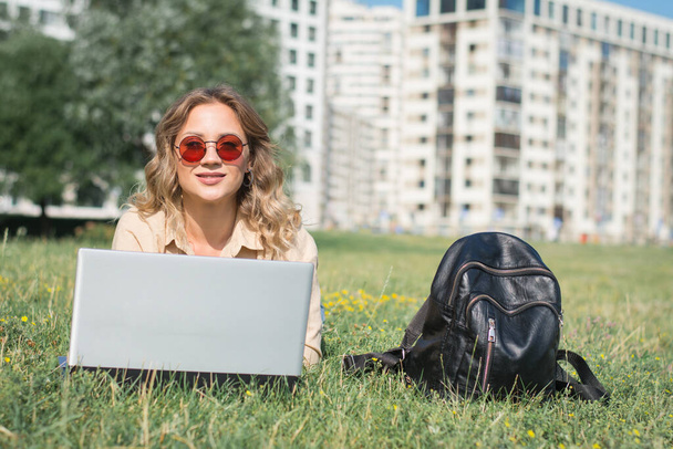 young female college student reading info on her laptop on a campus lawn - Foto, Bild