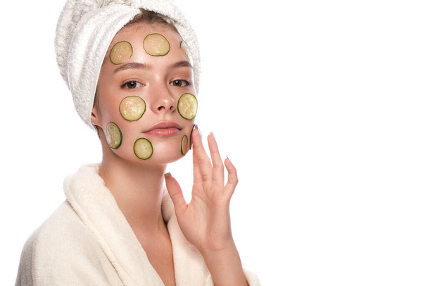 Beautiful tender young girl in a white towel with clean fresh skin posing in front of the camera with a mask of cucumbers on the face. Beauty face. Skin care. - 写真・画像