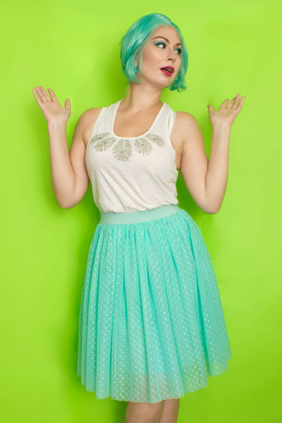 Portrait of a beautiful young woman with short blue hair in a studio on a green background. Mid-length romantic skirt and white blouse - Foto, Bild