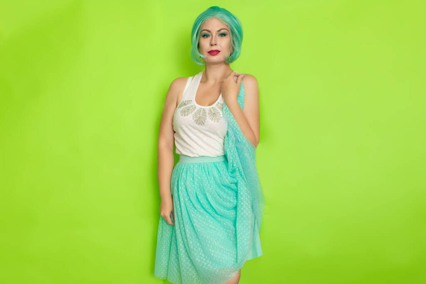 Portrait of a beautiful young woman with short blue hair in a studio on a green background. Mid-length romantic skirt and white blouse - Fotoğraf, Görsel