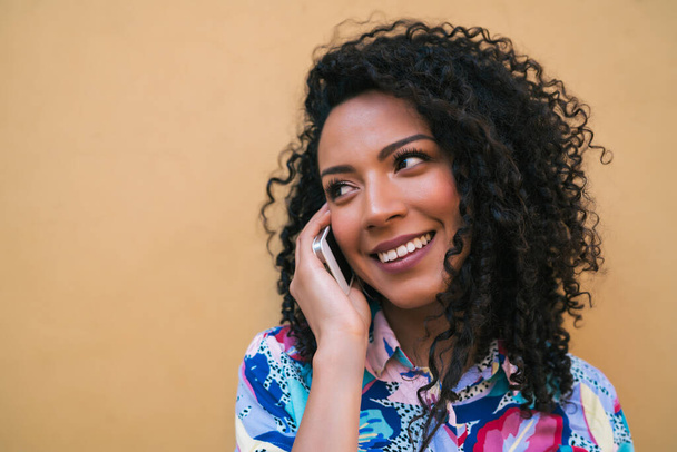 Egy fiatal afro nő portréja, aki sárga háttérrel beszél telefonon. Kommunikációs elv. - Fotó, kép