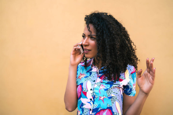 Portrait of young afro woman talking on the phone against yellow background. Communication concept. - Photo, Image