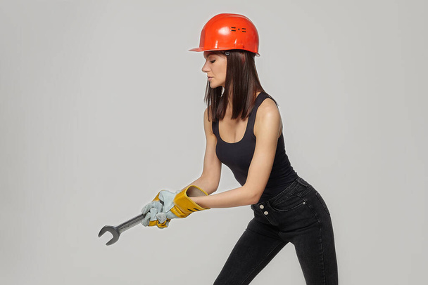 Construction girl in an orange helmet. holding a spanner. Posing while working twisting the imaginable bolt.. - Photo, Image