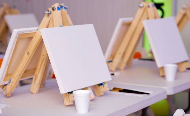 several easels prepared for a lesson with a set of brushes  - Photo, Image