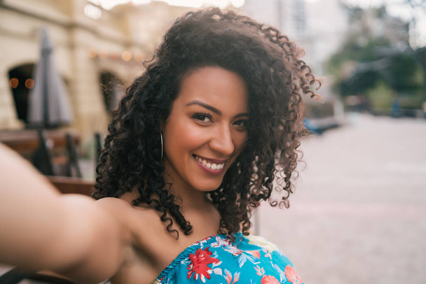 Portret van een jonge Afro-Amerikaanse vrouw die buiten een selfie maakt op straat. Genieten van het leven. Levensstijl concept. - Foto, afbeelding