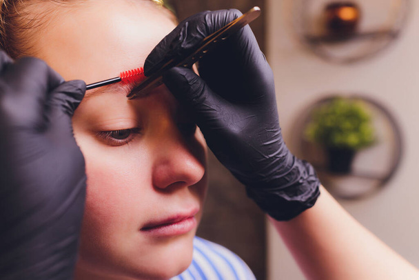 Make-Up. Beautician Hands Doing Eyebrow Tattoo On Woman Face.Permanent Brow Makeup In Beauty Salon. Closeup Of Specialist Doing Eyebrow Tattooing For Female. Cosmetology Treatment. - Zdjęcie, obraz