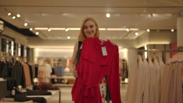 Dziewczyna shopper znaleźć czerwoną sukienkę swoich marzeń w sklepie odzieżowym - Materiał filmowy, wideo