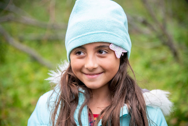 Χαριτωμένο κορίτσι weraing καπέλο κατά τη διάρκεια μιας κρύας ημέρας υπαίθρια. Χαμογελώντας σε κάποιον. - Φωτογραφία, εικόνα