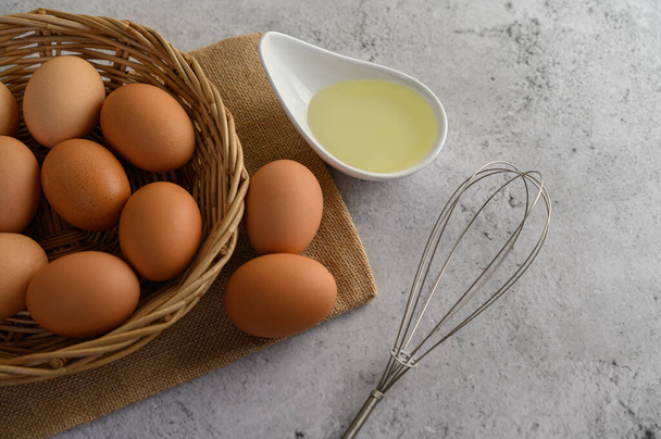 袋の布に卵を選択的に焦点を当て、ウィッカーバスケットとガラスボウルに多くの卵、床に置かれた油と卵泡立て器、料理やデザートの準備、コピー - 写真・画像