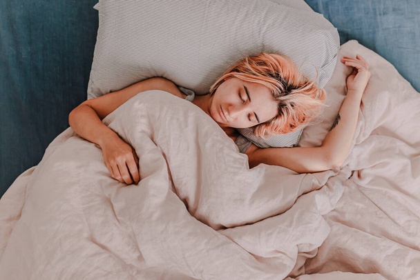 Young woman is relaxing in bed. Day off. Bedtime. Early morning light. White, beige, grey. Light and bright. Morning ritual. Apartment lifestyle living. Cozy bed linen. Taking a nap, sleep. Relaxed - Фото, изображение
