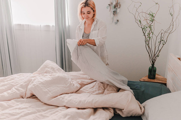Young pretty woman is making a bed. Fresh bedding linen. Put on pillow cover. Light and bright room. Beige, white, grey. Doing home improvement. Cleaning and organizing. Cozy house. Apartment living. - Foto, imagen