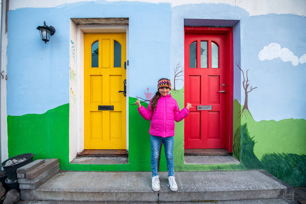 Schattig jong meisje dragen hoofd sjaal in de voorkant van twee mooie kleurrijke huis deuren. - Foto, afbeelding