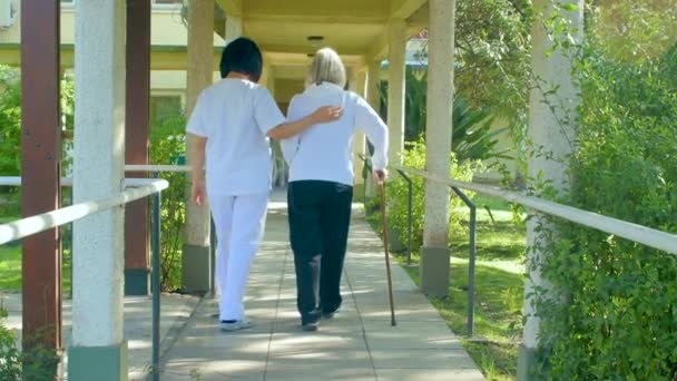 Медсестра помогает пожилой женщине с костылями в больнице. Вид сзади
 - Кадры, видео