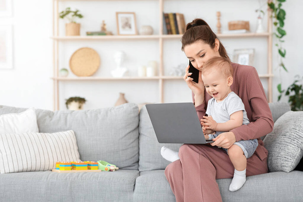 Εξισορρόπηση εργασίας και μητρότητας. Γυναίκα που χρησιμοποιεί κινητό και φορητό υπολογιστή ενώ κρατά το μωρό - Φωτογραφία, εικόνα