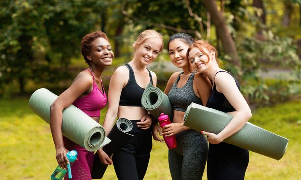 Retrato de diversas chicas con colchonetas de yoga antes de su clase de deportes en el parque
 - Foto, Imagen