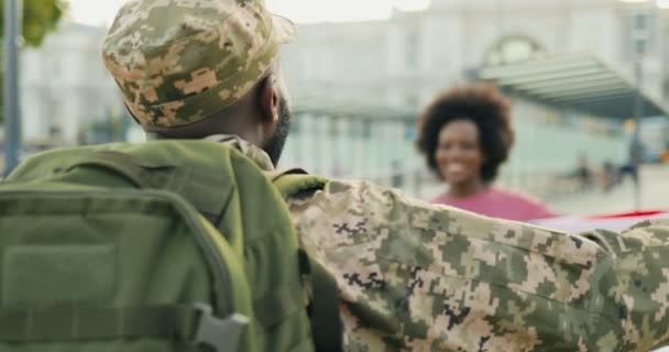 Gelukkige jonge Afro-Amerikaanse koppel ontmoeten en knuffelen op straat. Knappe mannelijke soldaat in uniform die terugkomt uit het leger en een ontmoeting heeft met een mooie vriendin met de vlag van de VS. Oorlogsdienst keert terug. - Video