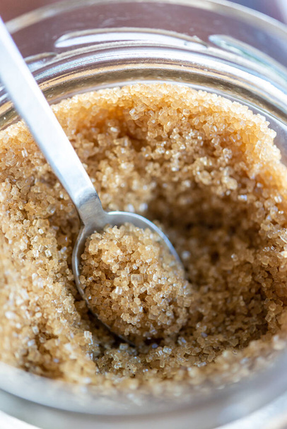 Spoon of brown organic sugar in glass sugar bowl. - Photo, Image